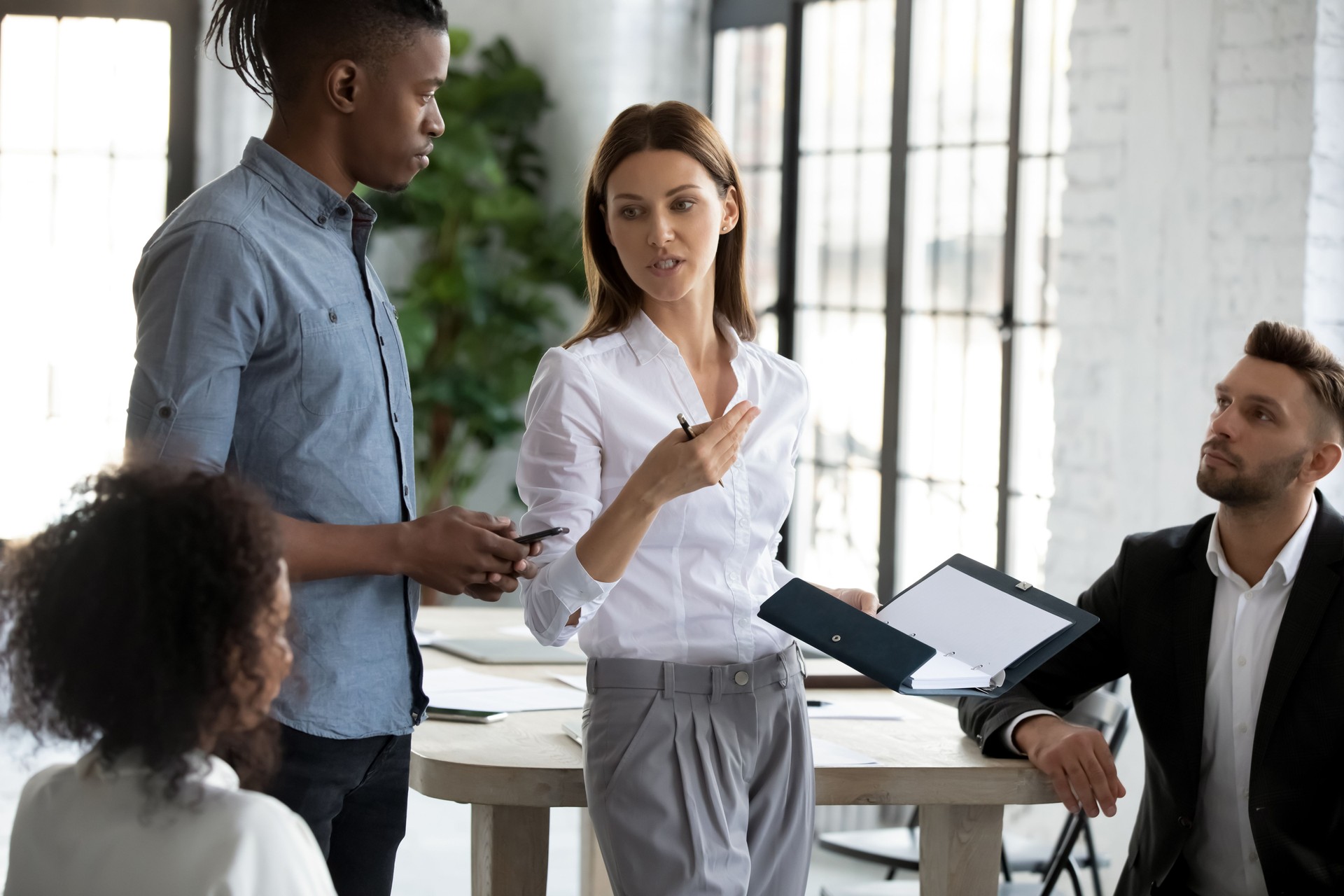 Confident serious businesswoman in suit standing telling diverse employees.